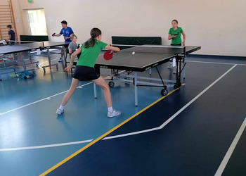zdjęcie przedstawia uczestników biąrcych udział w turnieju tenisa stołowego podczas rozgrywek